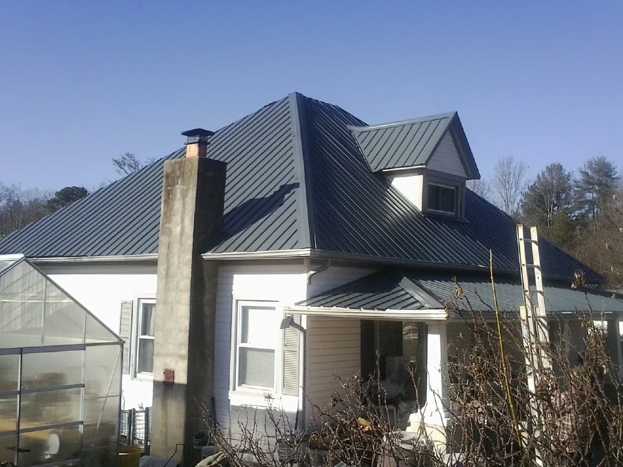 Dark blue standing seam metal roof on a white farmhouse with dormer in Stoneham