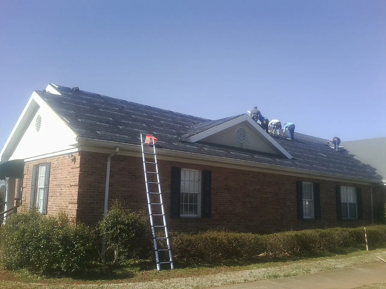 Crew tearing shingles off a brick ranch roof with a ladder set — Metal Roof Repair work by our crew in Stoneham