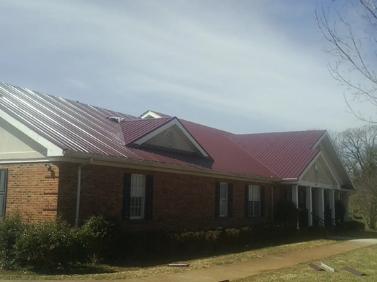 Red metal roof with gabled entries on a long brick building, from a Hail Damage Roof Repair job in Stoneham