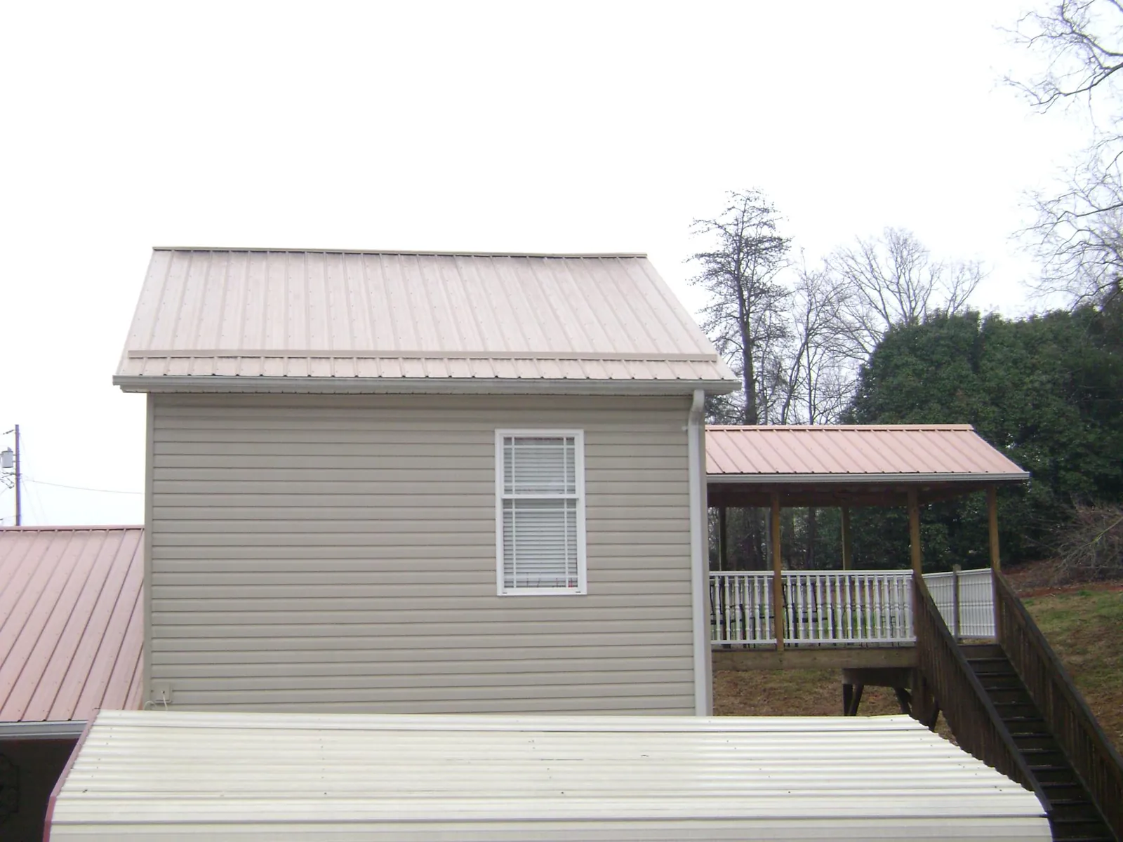 Tan metal roofs on a two story addition and attached porch, from a Roof Replacement job in Stoneham